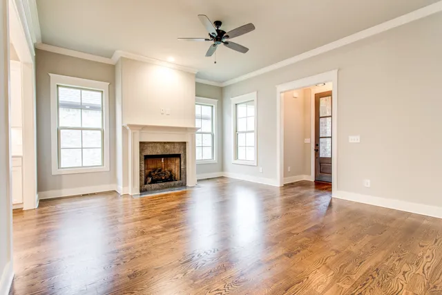 an empty room with wooden floor fireplace and windows
