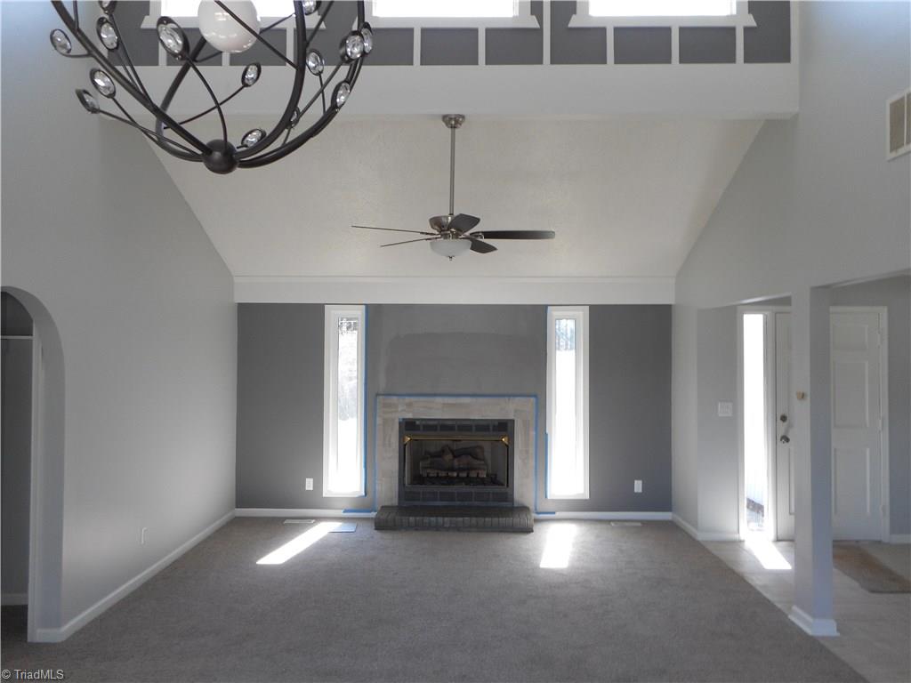 5929 Styers Ferry Road Clemmons, NC 27012 - Photo 2 of 28 Here we are inside the home looking into the open living room from the dining room area. Here we have the nice and cozy fireplace with gas logs that can also help to warm your home on a cool winters day. You also have new carpet, fresh new paint, five windows for natural lighting, the ceiling fan with light and the vaulted ceiling.