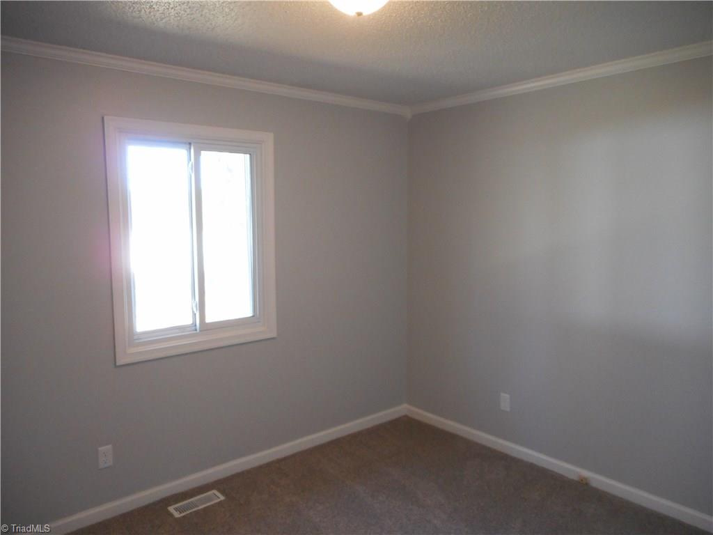 5929 Styers Ferry Road Clemmons, NC 27012 - Photo 25 of 28 In this view we are looking into bedroom three where we can see the fresh new paint, new carpet flooring, crown molding and a window for natural lighting.