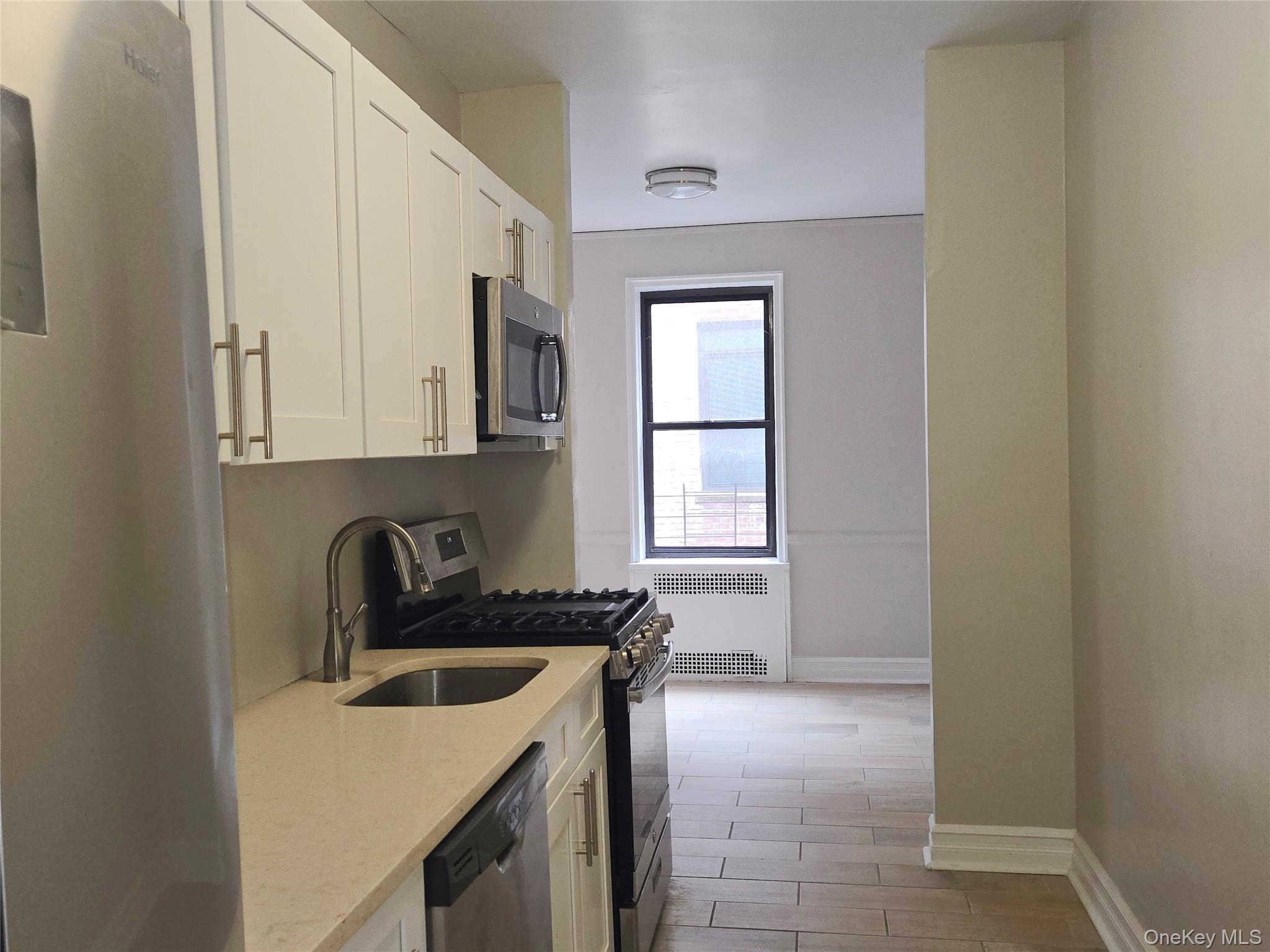 55 East 190th Street, Unit 45 Bronx, NY 10468 - Photo 8 of 13 Kitchen with stainless steel appliances, light stone counters, white cabinetry, radiator heating unit, and wood tiled floors