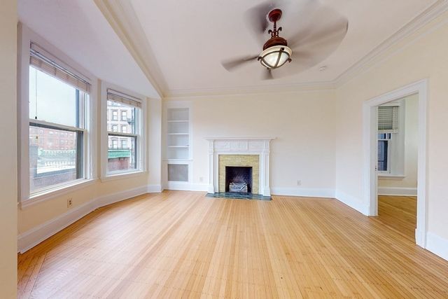 a view of an empty room with wooden floor fireplace and a window