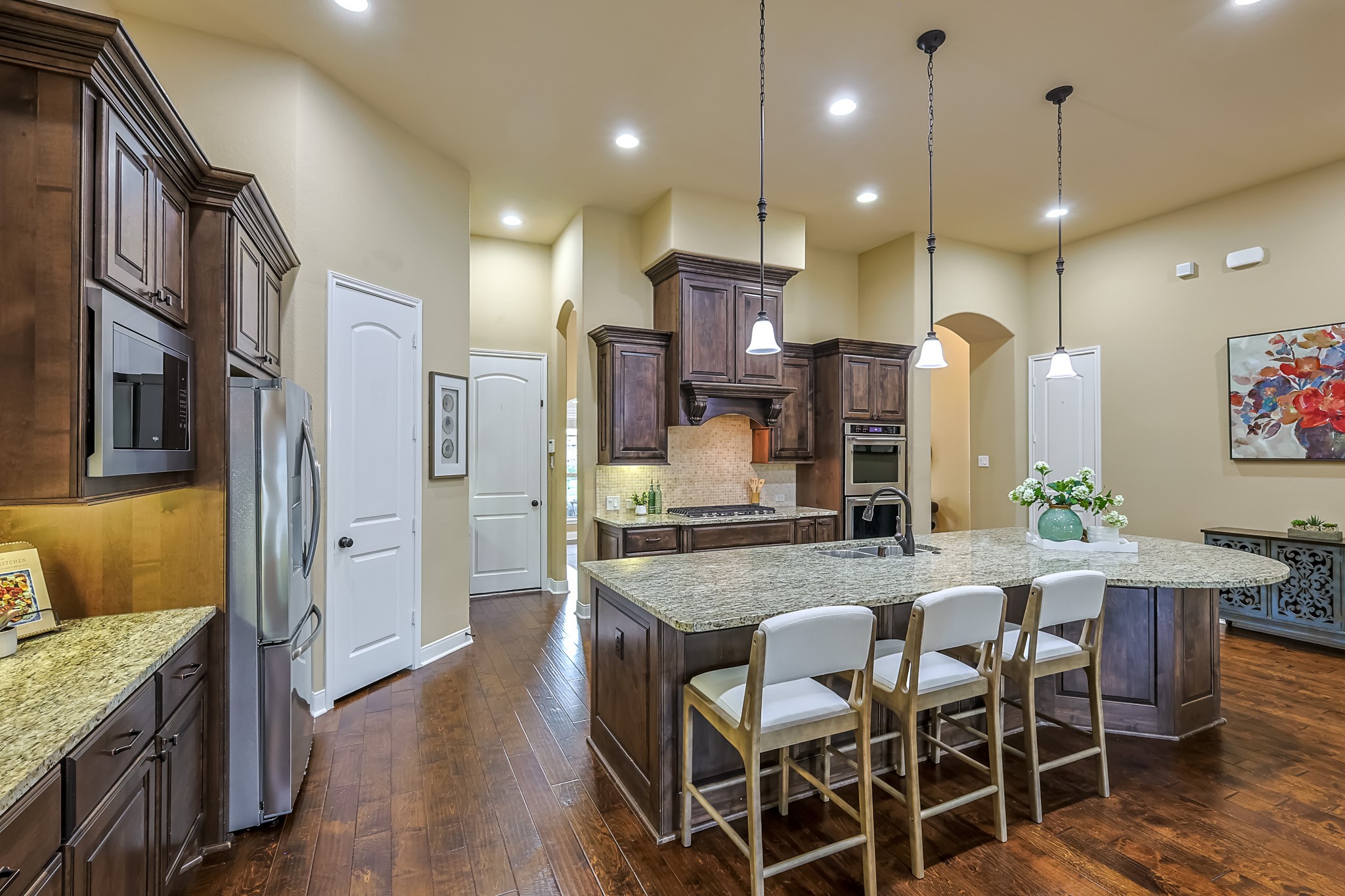 515 Mill Creek Road Pinehurst, TX 77362 - Photo 19 of 48 This kitchen features a spacious layout with dark wood cabinetry, granite countertops, and a large central island with seating. Stainless steel appliances and pendant lighting add a modern touch, while the warm hardwood floors create a cozy atmosphere.
