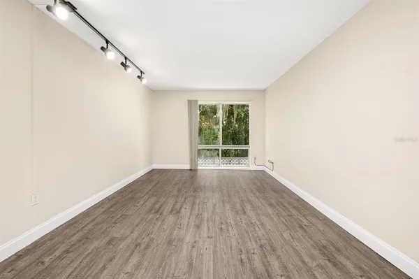 a view of an empty room with wooden floor and fan