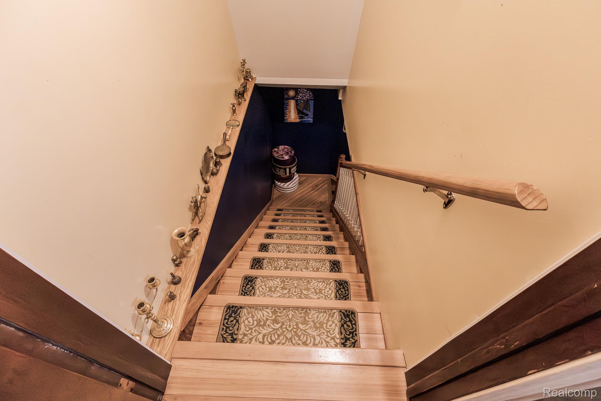 8197 Irish Road Millington, MI 48746 - Photo 33 of 38 Wood-finish staircase featuring individual stair treads with patterned runners, a natural wood handrail, and a contrasting dark wall accent