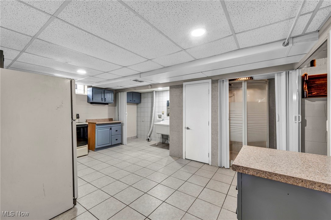 10927 Granger Road Cleveland, OH 44125 - Photo 22 of 33 Finished basement featuring freestanding refrigerator, light tile patterned floors, and a drop ceiling