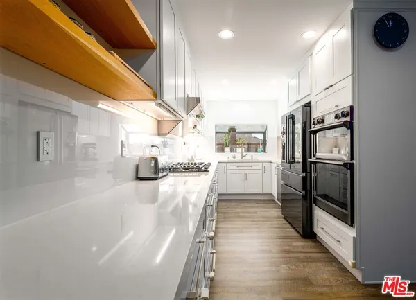 a kitchen with stainless steel appliances granite countertop a refrigerator a oven a sink and white cabinets with wooden floor