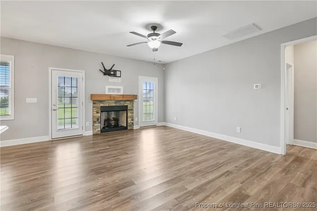 an empty room with wooden floor fireplace and windows