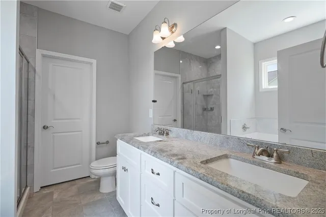 a bathroom with a granite countertop double vanity sink a mirror and a toilet