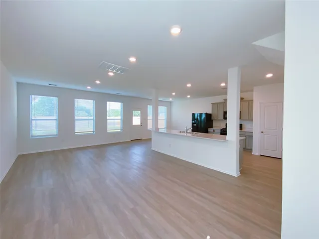 a view of an empty room with wooden floor and a kitchen