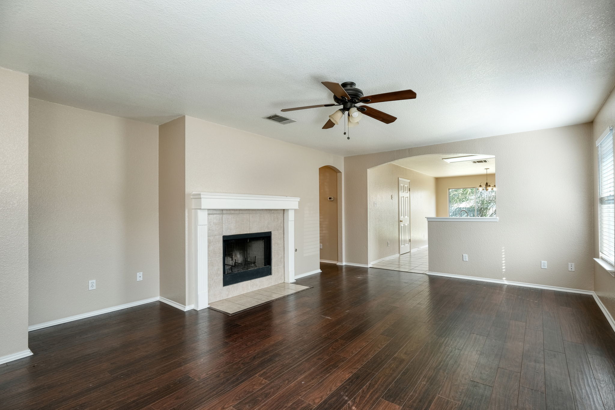 124 Hunter Rex Way Kyle, TX 78640 - Photo 3 of 14 Spacious living area featuring wood-finish flooring, a tiled fireplace with white mantle, and an arched entryway