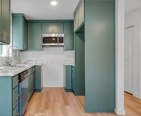 a view of an empty room with wooden floor and a kitchen