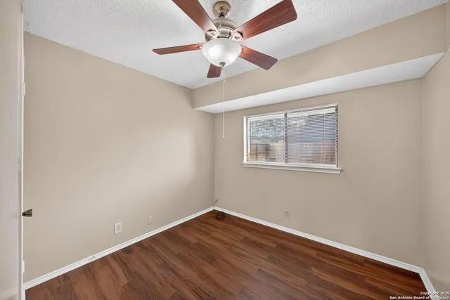 an empty room with wooden floor chandelier fan and windows