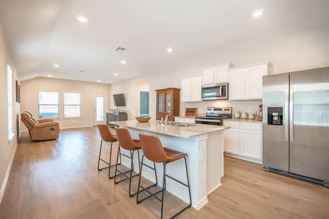 a kitchen with stainless steel appliances granite countertop a refrigerator a stove a sink a dining table and chairs with wooden floor