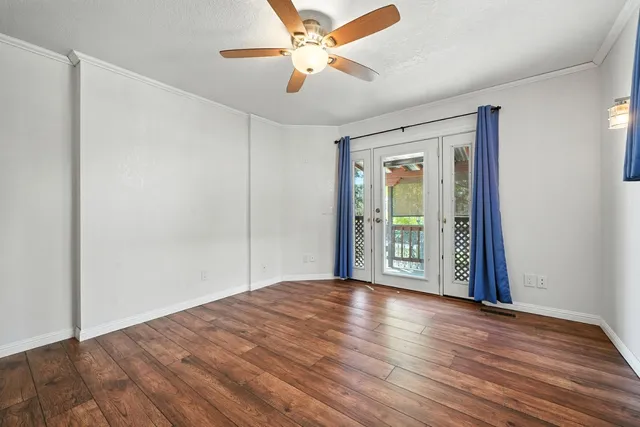 an empty room with wooden floor chandelier fan and windows