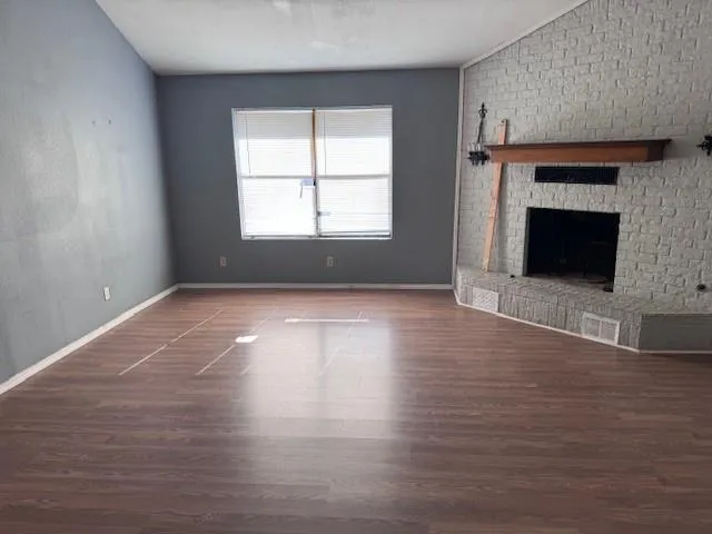 an empty room with wooden floor fireplace and windows