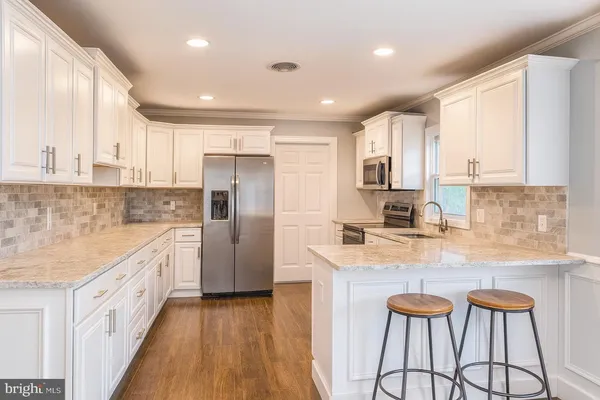 a kitchen with stainless steel appliances granite countertop a refrigerator a sink dishwasher a stove and white countertops with wooden floor