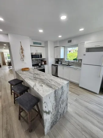 a kitchen with stainless steel appliances kitchen island granite countertop a refrigerator a stove a sink a dining table and chairs with wooden floor