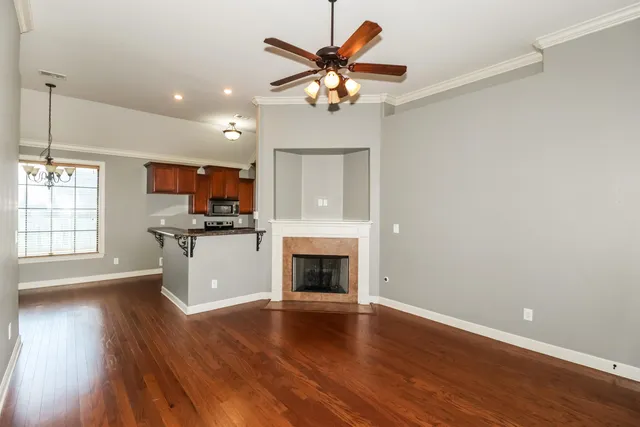 an empty room with wooden floor a kitchen view and a fireplace