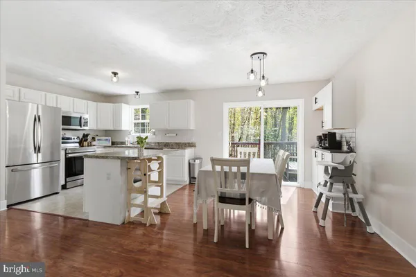 a kitchen with stainless steel appliances a dining table chairs refrigerator and cabinets