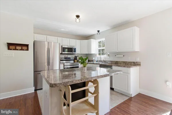 a kitchen with stainless steel appliances granite countertop a refrigerator a stove a sink dishwasher and white cabinets with wooden floor