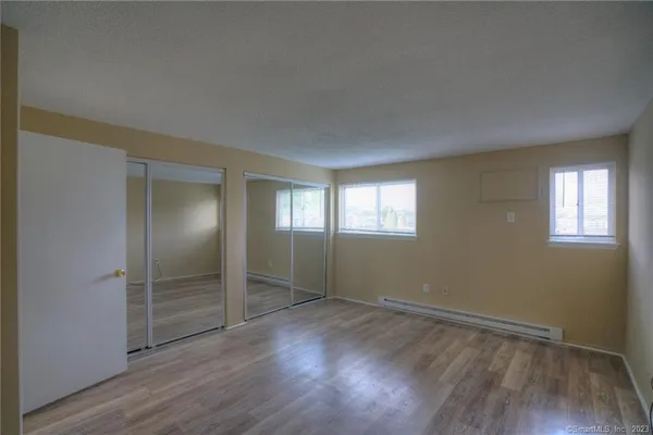 an empty room with wooden floor closet and windows