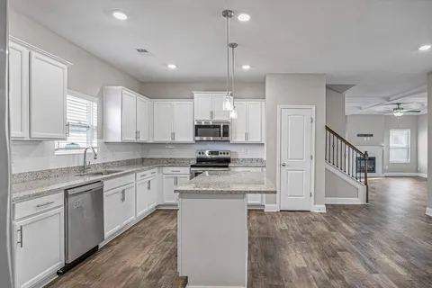 a kitchen with stainless steel appliances granite countertop a stove top oven a sink a refrigerator and white cabinets with wooden floor