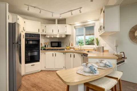 a kitchen with stainless steel appliances kitchen island granite countertop a refrigerator a sink a stove and white cabinets with wooden floor