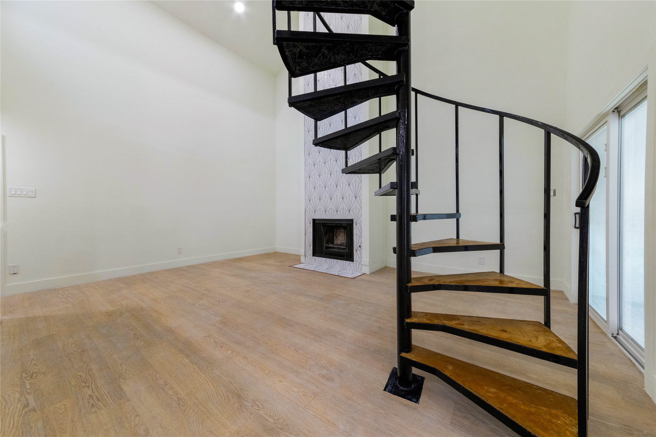 8807 Merion Circle Austin, TX 78754 - Photo 17 of 18 A stylish spiral staircase and modern fireplace accent this open-concept living area with light wood flooring.