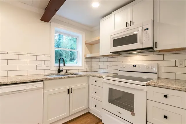 a kitchen with granite countertop white cabinets appliances and a sink