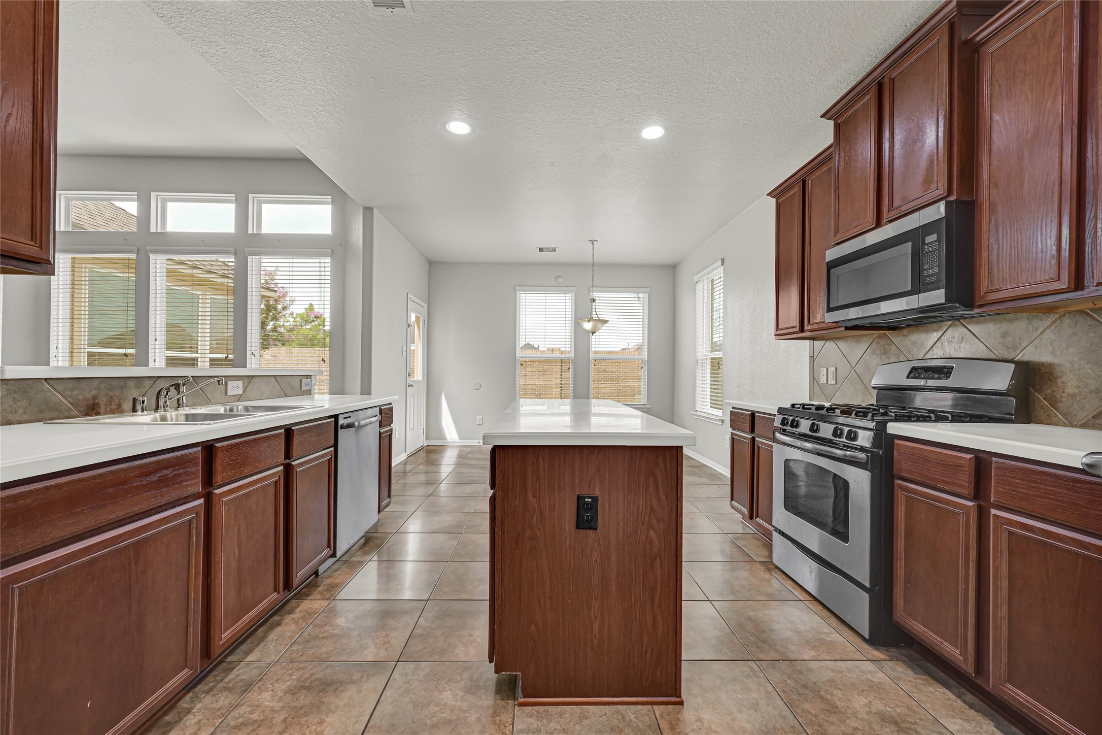 4702 Sedgewood Drive Rosenberg, TX 77471 - Photo 15 of 24 Spacious kitchen with modern appliances, ample natural light, and stylish tile flooring. Features dark wood cabinetry, a central island, and large windows for a bright, inviting atmosphere.