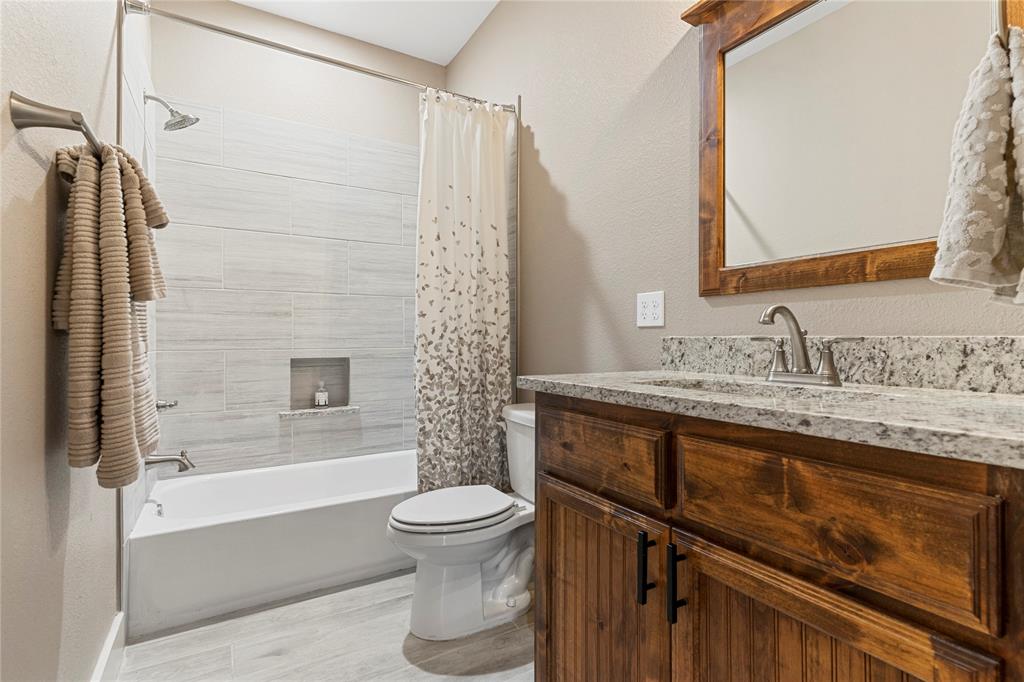 139 Kriston Lane Springtown, TX 76082 - Photo 16 of 39 Bathroom featuring a white tub, light-toned tile surround with a recessed niche, wood-finish vanity with a granite countertop, and light wood-finish flooring