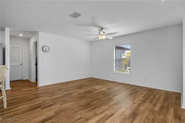 an empty room with wooden floor chandelier fan and windows