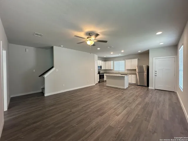 a view of an empty room with wooden floor and a ceiling fan
