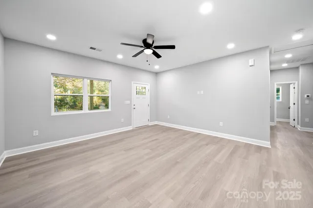 an empty room with wooden floor ceiling fan and windows
