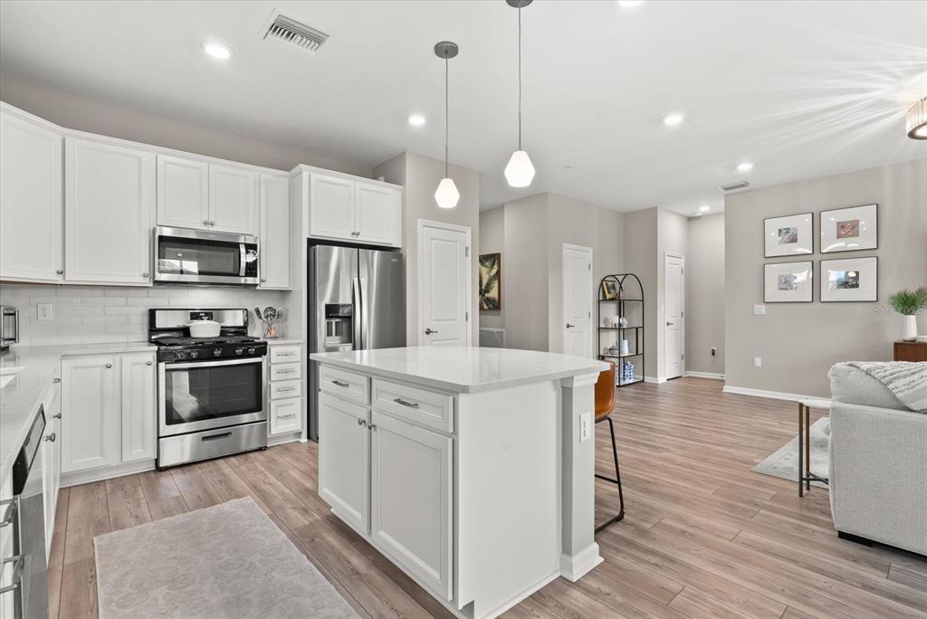 3310 Chestertown Loop Bradenton, FL 34211 - Photo 10 of 71 a kitchen with stainless steel appliances kitchen island a refrigerator a stove a sink a dining table and chairs with wooden floor