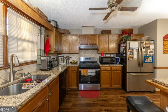 a kitchen with stainless steel appliances granite countertop a refrigerator a sink dishwasher a stove and a dining table with wooden floor