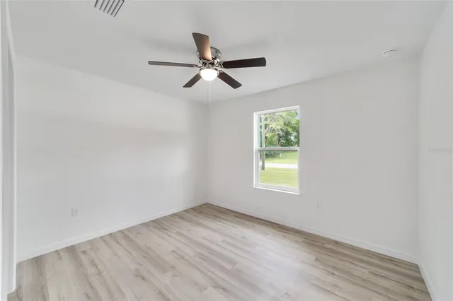 an empty room with wooden floor and ceiling fan