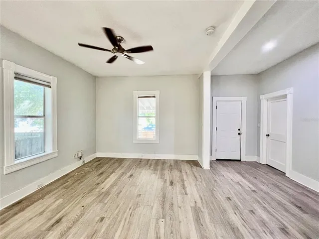 an empty room with wooden floor a ceiling fan and windows