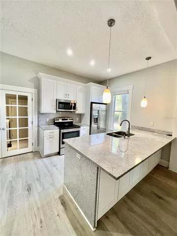 a kitchen with stainless steel appliances granite countertop a sink dishwasher a refrigerator and white cabinets with wooden floor