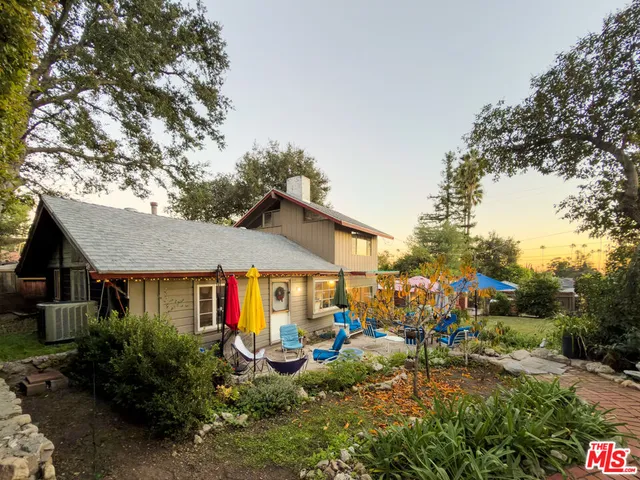 a view of a white house with large trees and plants