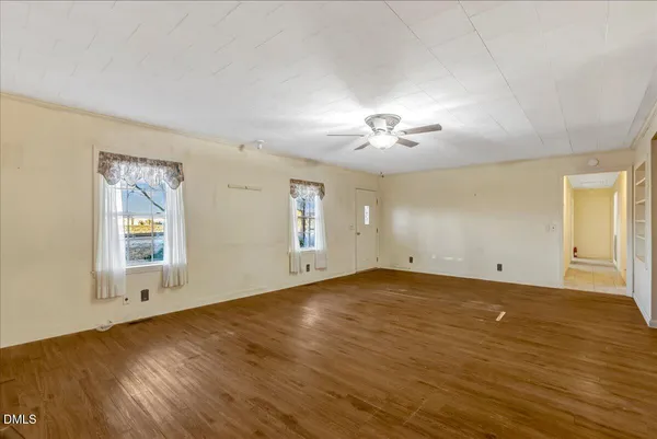 an empty room with wooden floor chandelier and windows