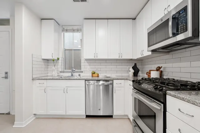 a kitchen with stainless steel appliances granite countertop white cabinets a sink and a stove