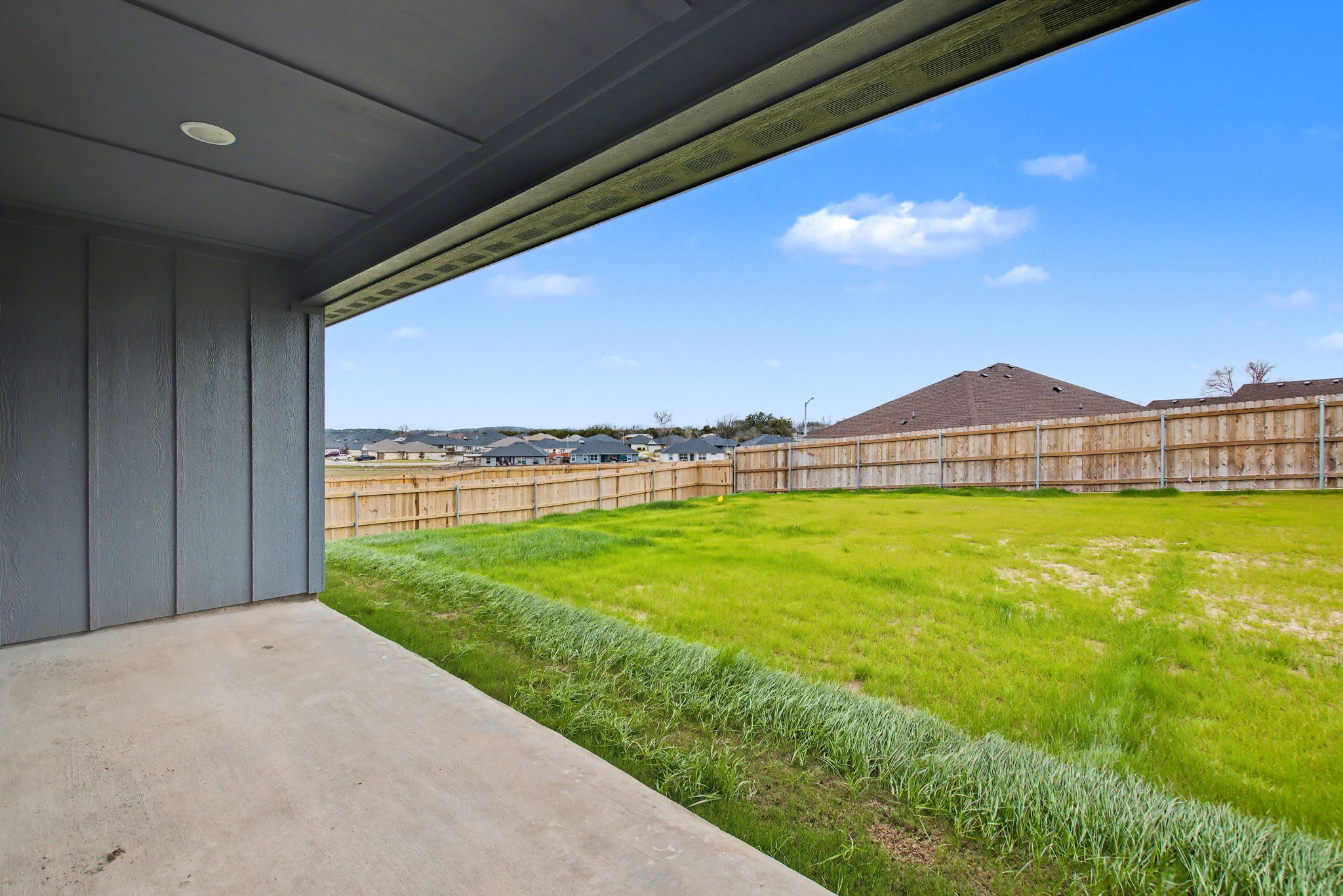 206 Water Wl Road Burnet, TX 78611 - Photo 24 of 25 A covered concrete patio overlooks a spacious grassy yard enclosed by wooden fencing.
