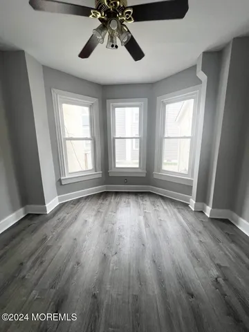 an empty room with wooden floor chandelier fan and windows