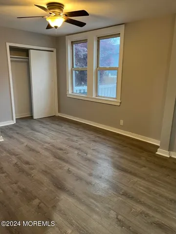 an empty room with wooden floor fan and windows
