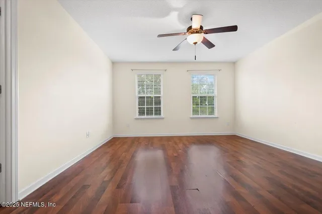 an empty room with wooden floor ceiling fan and windows