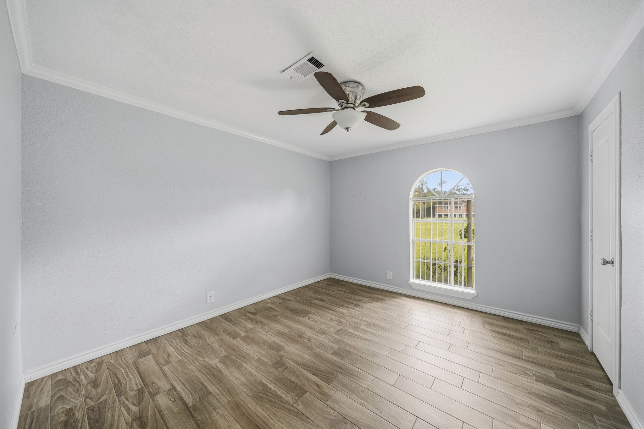 302 Country Road 893 Angleton, TX 77515 - Photo 16 of 26 Bright room with light gray walls and wood-look tile flooring. Features a ceiling fan and an arched window with a view of the lawn, perfect for a cozy bedroom or office.
