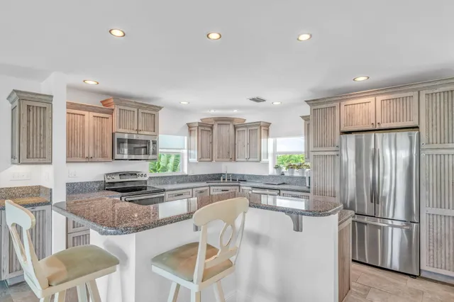 a kitchen with stainless steel appliances granite countertop a refrigerator a stove a sink a dining table and chairs