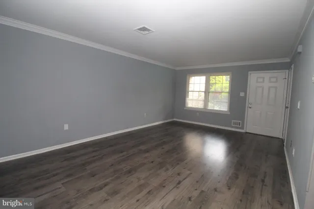 a view of an empty room with wooden floor and window