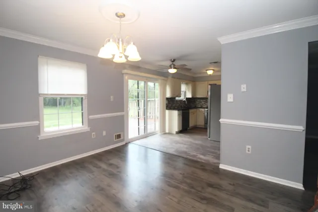 an empty room with wooden floor chandelier and windows